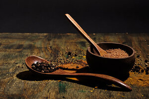 Pepper and coriander with wooden bowl and wooden spoon with spices on wood