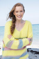 Young, blonde woman in a yellow jumper with coloured stripes by the sea