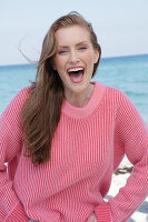 Good-humoured young blond woman in pink jumper by the sea