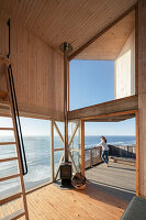 View from living area to entrance and terrace of a wooden house with sea view, woman in the background