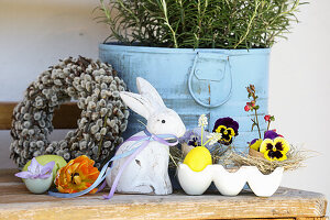 Osterdekoration mit Kranz aus Palmkätzchen, Osterhase und Stiefmütterchen im Eierkarton