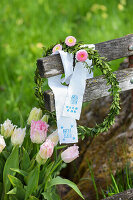 Holzbank mit Buchskranz und Gänseblümchen (Bellis), bestempelte Stoffreste mit Ostergruß und Tulpen (Tulipa)