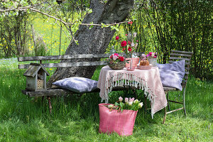 Gartentisch mit Frühlingsblumen und Gugelhupf, Tasche mit Tulpen im Gras