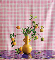 Citrus branches in a decorative vase in front of a gingham background
