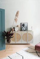 Cabinet with rattan fronts and decorative elements next to houseplant