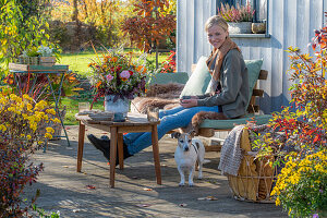 Frau auf herbstlicher Terrasse mit Hund und Blumendekoration