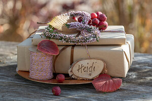 Two gifts decorated with flower hearts made of heather, ornamental apple and name plate on a garden table