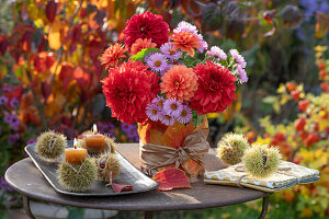 Herbstblumenstrauß aus Dahlien (Dahlia) und Astern, Kerzen in Schalen von Esskastanien (Castanea Sativa) und Herbstlaub