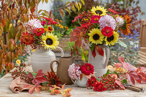 Herbstliche Blumensträuße auf der Terrasse mit Dahlien (Dahlia), Sonnenblume (Helianthus), Zinnien (Zinnia), Hagebutten, Jungfernreben (Parthenocissus)