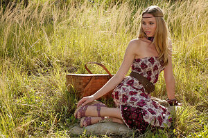 Blonde Frau im schulterfreiem Sommerkleid mit Picknickkorb auf der Wiese