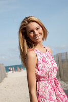Blonde woman in pink and white summer dress on the beach