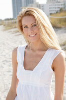 Blonde Frau in weißem Sommerkleid am Strand