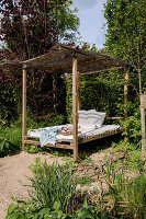 Gartenbett mit Überdachung, Kissen und Decken umgeben von Grünpflanzen