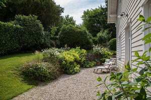 Well-tended garden and gravel terrace in front of house with wood paneling