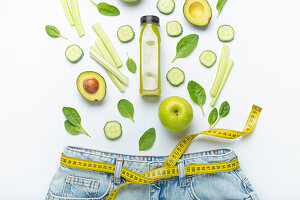 Grünes Obst, Gemüse und Smoothie fallen in Jeans mit gelbem Maßband als Gürtel