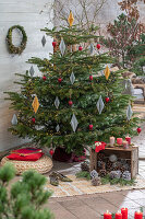 Weihnachtsdeko im Wintergarten, Kerzen, Papieranhänger und bemalte Zapfen vor geschmücktem Christbaum