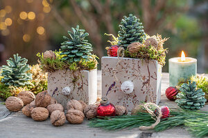 Adventsdeko auf Terrassentisch mit Kerze, Christbaumkugeln, Nüssen, Kiefernzweigen, Zapfen und Moos im Keramiktopf