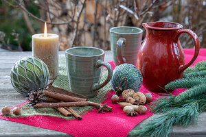 Weihnachtsdeko am Terrassentisch mit Kerze, Kaffeetassen, Tannenzweig, Christbaumkugeln, Zimtstangen und Nüssen