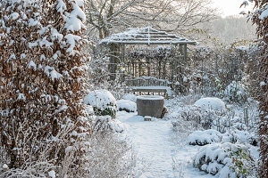 Verschneite Beete im winterlichen Garten und Pavillon mit Sitzplatz