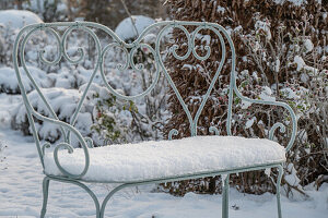 Verschneite Gartenbank im winterlichen Garten