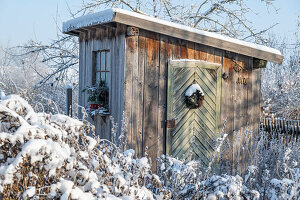 Holzschuppen im verschneiten Garten mit Winterdekoration