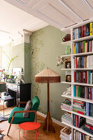 Green armchair and red side table in front of light green painted wall with nature motif in the living room