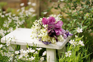 Bouquet of tulips (Tulipa), lily of the valley (Convallaria) and bluebells (Hyacinthoides) on a stool in the garden