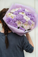Frau hält Blumenstrauß mit hellvioletten Nelken (Dianthus) und Chrysanthemen (Chrysanthemum)