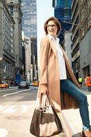 Young woman with glasses and a bag in a light coat on the street with skyscrapers