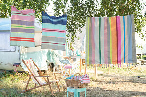 Striped towels on clothes line next to camping chair and camper