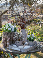 Saxifrage (Saxifraga arendsii), horned violet (Viola cornuta), in flower basket, in front of it Easter bunny, eggs and pussy willows on garden table