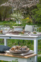 Gedeckter Tisch im Garten für Osterfrühstück mit Osternest und gefärbten Eiern in Eierbechern und Blumenstrauß in Etagere