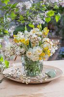 Bouquet of cowslip (Primula veris), rock pear (Amelanchier), daffodils 'Bridal Crown' (Narcissus) in glass vase and eggshell on garden table