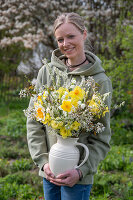 Young woman carrying a bouquet of rock pear (Amelanchier) branches, daffodils(Narcissus), bride's spirea and spring snowflakes in a jug