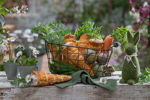 Blätterteigtüten im Ofen gebacken, gefüllt mit Karotten-Dill-Sauresahnesoße im Drahtkorb und gefärbten Eiern, Kräuter als Deko, Gänseblümchen in Tasse als Vase, Osterhasenfigur