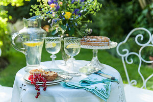 Sommerlicher Gartentisch mit Kuchen, Törtchen und Zitronenwasser