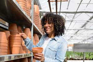 Smiling young woman in nursery at shelf with clay pots