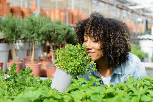 Smiling young woman in nursery smelling herb pot