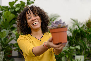 Lachende junge Frau in Gärtnerei präsentiert Sukkulente in Topf