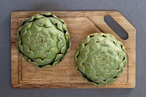 Two fresh artichokes on a wooden board