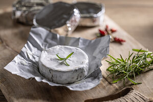 Brie cheese in aluminium foil with rosemary and chilli on a chopping board