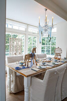 Bright dining area with wooden table, chairs with covers, wooden horse and chandelier