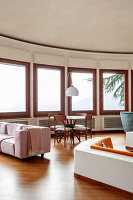 Round living room with many windows, round dining table and pink sofa