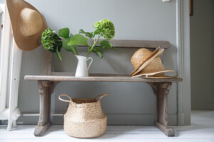 Wooden bench with straw hats, hydrangeas and woven basket under the bench