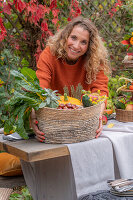 Frau hält Korb mit Zucchini, Kürbis, Äpfeln, Kastanien, Fenchelblüten und Mangold