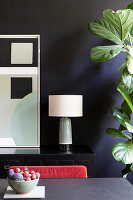 Black sideboard with table lamp and abstract artwork on black wall