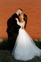 Bride and groom embracing against brick wall