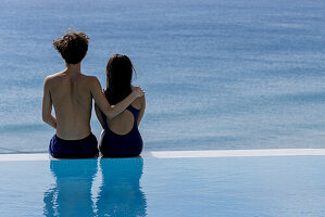 Young couple sitting at poolside looking at ocean