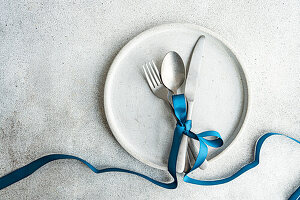 Top view of minimalist yet stylish Easter table setting, with cutlery tied together with blue ribbon on concrete plate, placed on gray table