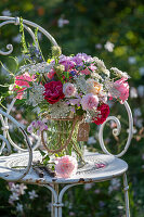 Bouquet of roses, wild carrot, flowering oregano, vetch, autumn anemone and bearded flower on iron chair